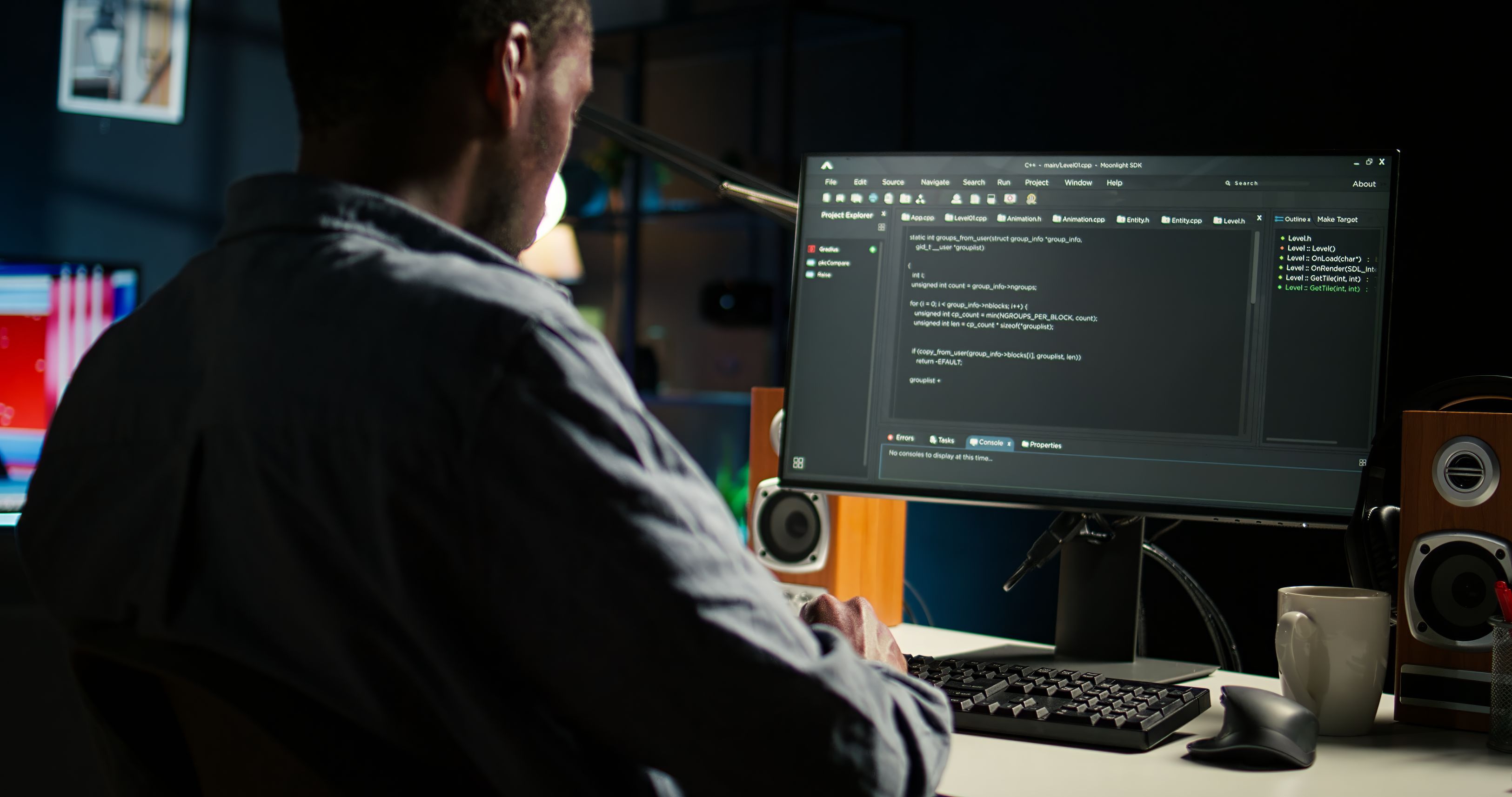 A software developer writes code on a computer monitor in a dimly lit workspace.